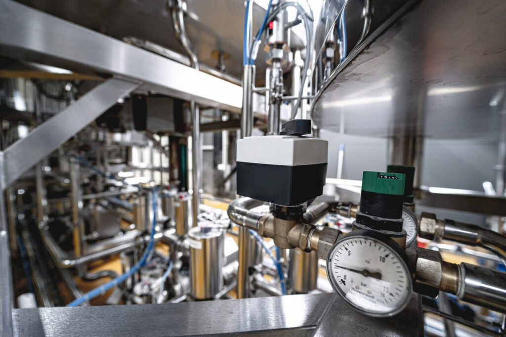 Gauge on a tank to measure usage with stainless steel pipes in a factory.