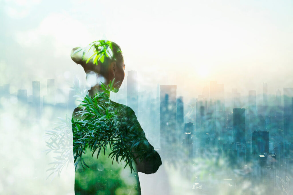 Person standing in contemplation in urban city with nature trees composite over her body.