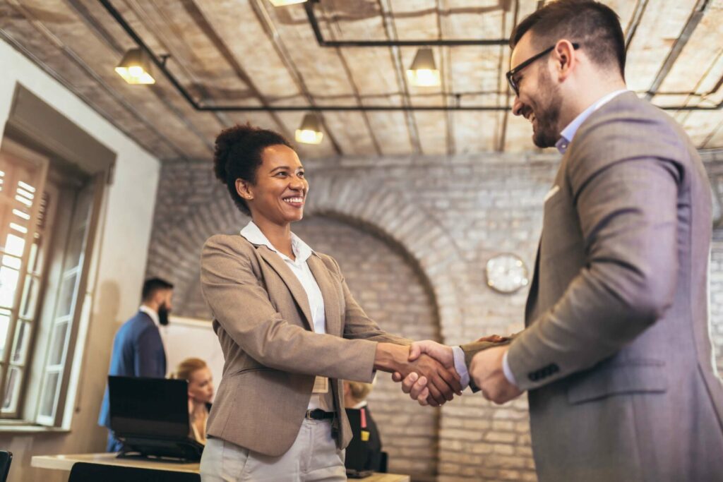Two people smiling and shaking hands in business clothes.
